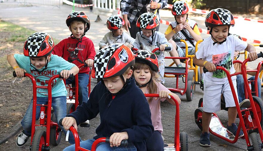 Mehrere Kinder fahren auf Laufrädern über einen Weg.