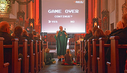 Weihbischof Rolf Lohmann steht vor den Gläubigen in der Mariä-Empfängnis-Kirche, im Hintergrund steht auf einer Leinwand das Motto des Gottesdienstes.