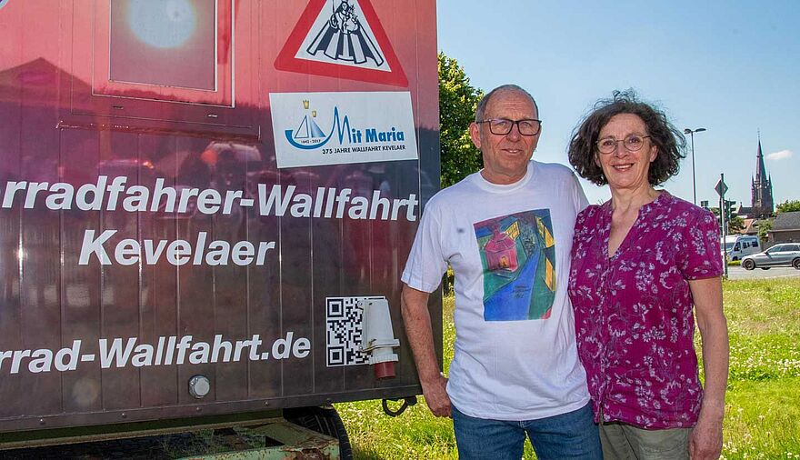 Ein Mann und eine Frau stehen neben einem Bauwagen, im Hintergrund ist die Marienbasilika in Kevelaer zu erkennen.