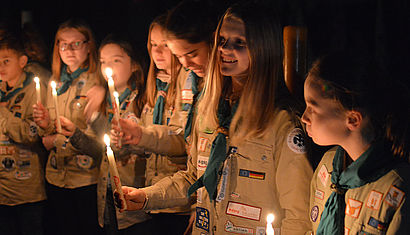 Mehrere Jugendliche in Pfadfinderkluft stehen im dunklen Dom und halten brennende Kerzen in der Hand.