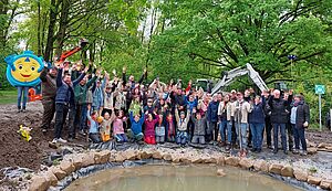 Bischof Dr. Felix Genn und die jungen Menschen der Aktionsgruppe stehen an dem neu angelegten Teich und winken.