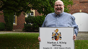 Markus J. König hält ein Schild mit der Adresse seiner Stiftung in den Händen