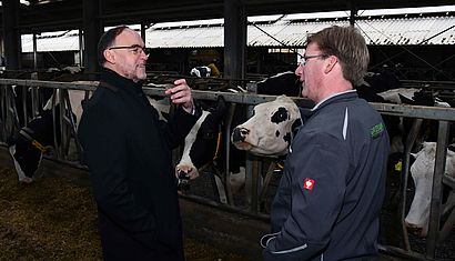Weihbischof Rolf Lohmann steht mit Landwirt Thomas Cleven in einem Kuhstall.
