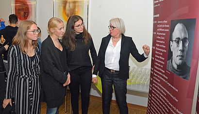 Vor einer Infotafel mit dem Bild von Karl Leisner stehen drei Schülerinnen und Monika Kaiser-Haas im Gespräch.