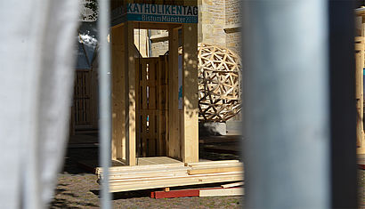 Blick durch den Bauzaun an der Plane vorbei auf den Überwasserkirchplatz auf die Bistumspräsentation.