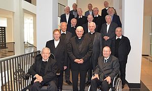 Die 16 Weihejubilare stehen gemeinsam mit Bischof Dr. Felix Genn auf der Treppe im Eingangsbereich des Priesterseminars Borromaeum.