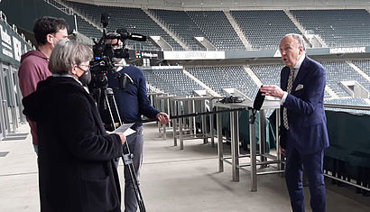 Eine Frau interviewt mit einem Kamerateam einen Mann in einem Sportstadion.