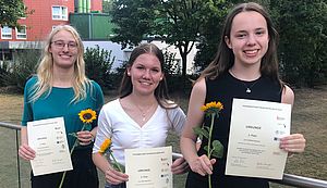 Drei junge Frauen stehen nebeneinander. Jede hält eine Urkunde und eine Sonnenblume in den Händen. Drei junge Frauen stehen nebeneinander. Jede hält eine Urkunde und eine Sonnenblume in den Händen.