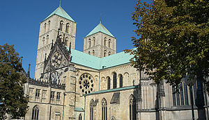 Der St. Paulus-Dom Münster, teilweise verdeckt von grün belaubten Bäumen auf dem Domplatz.