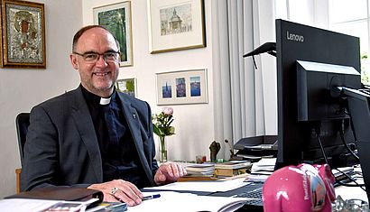 Weihbischof Rolf Lohmann sitzt an seinem Schreibtisch vor einem Computerbildschirm.