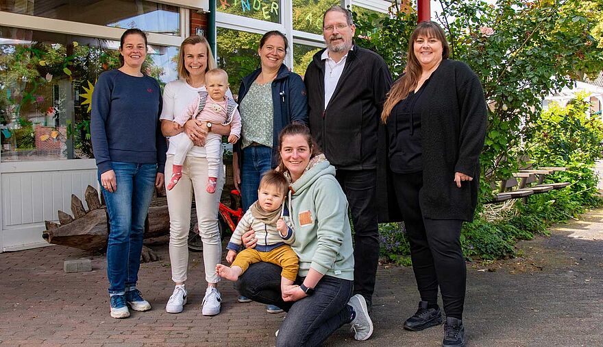 5 Frauen, davon 2 mit kleinen Kindern auf dem Arm, und ein Mann stehen vor dem Eingang eines Kindergartens.