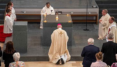 Mehrere Menschen knien um einen Altar, auf dem fünf Feuer brennen.