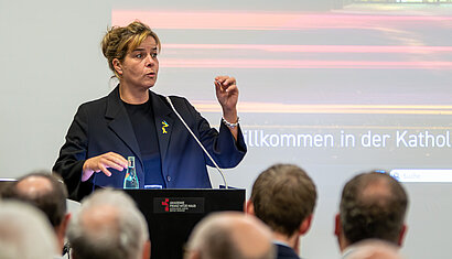 Ministerin Mona Neubaur steht an einem Rednerpult und gestikuliert, während sie spricht.