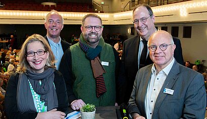 Eine Frau und vier Männer stehen zusammen auf einer Bühne und lächeln.