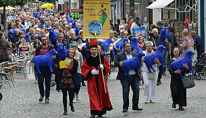 Über die Hauptstraße von Kevelaer ziehen zahlreiche Menschen in Richtung Basilika, einige von ihnen tragen ein blaues Kunststoffschaf im Arm.
