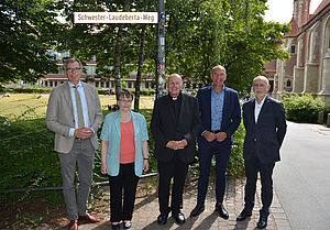Unter dem Straßenschild mit der Aufschrift "Schwester-Laudeberta-Weg" stehen (von links) Dr. Eduard Hüffer, Schwester Susanne Kamperdick, Felix Genn, Georg Lunemann und Johannes Balthesen. 		