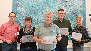 Vier Männer und eine Frau stehen nebeneinander vor einer weißen Wand mit einem blauen Bild. In ihren Händen halten sie Schilder auf denen steht: „Öko-Faire Kirchengemeinde Pfarrei Liebfrauen Bocholt"