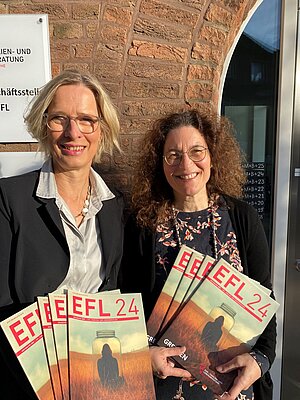Andrea Beer und Andrea Staochon-Groth stehen vor dem EFL-Gebäude in Münster. Sie halten mehrere Exemplare des EFL-Jahresberichts 2024 in den Händen.