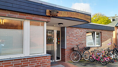 Auf dem Bild ist der Eingangsbereich der Kita von außen zu sehen mit dem Schild "Kita St. Pius".