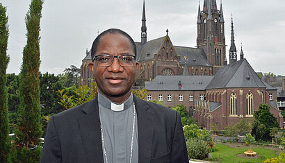 Porträt von Erzbischof Lompo mit der Marienbasilika in Kevelaer im Hintergrund.