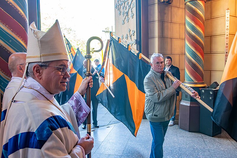 Ein Bischof sieht zu, wie Männer, die Fahnen der Kolpingsfamilien tragen, in eine Kirche einziehen.