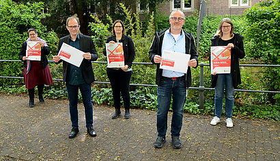 Die Mitglieder des KODA-Wahlvorstands halten Wahlplakate und Umschläge in die Kamera. 