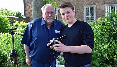 Dr. Peter Hahnen und sein Sohn Vincent, der eine Kamera in den Händen hält, stehen im Kräutergarten von Kloster Kamp.