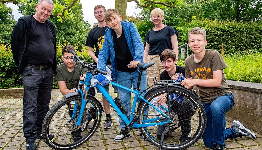 Mehrere Personen stehen oder knieen hinter einem blauen Fahrrad.