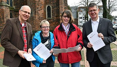 Michael Beermann, Ellen Rütten, Petra Hähn und Propst Johannes Mecking stehen nebeneinander an der Stiftskirche und halten Kopien des ISK in den Händen.