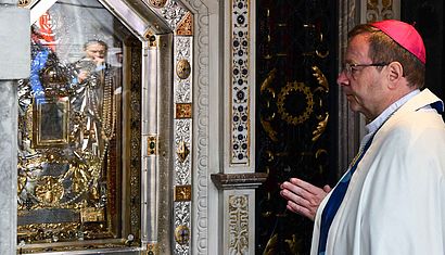 Bischof Bätzing steht mit gefalteten Händen rechts in der Gnadenkapelle und schaut nach links auf das Gnadenbild.