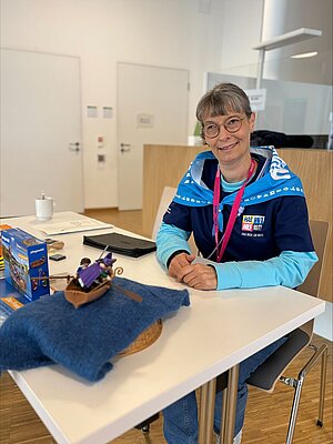 Eine lächelnde Frau sitzt an einem Tisch, auf dem Infomaterialien liegen.