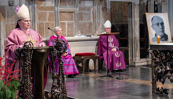 Bischof Meier steht am Ambo im Xantener Dom, rechts ist das Porträt von Karl Leisner aufgestellt.