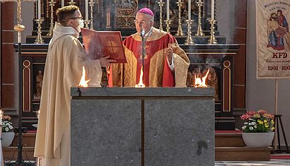 Bischof Felix Genn steht betend an einem Altar, auf dem Flammen brennen.