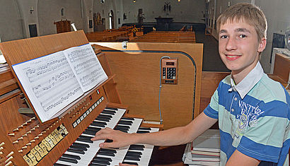 Der 16-jährige Benedict Jaeger sitzt an der Kirchenorgel von Mariä Himmelfahrt in Wesel, seine Finger liegen auf dem Manual, im Hintergrund sieht man Kirchenbänke und den Altarraum.