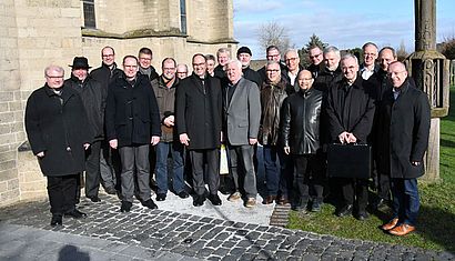 Zahlreiche Männer stehen vor einer Kirche in der Sonne.