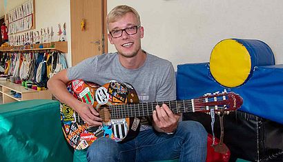 Ein Mann sitzt mit einer Gitarre im Kindergarten.