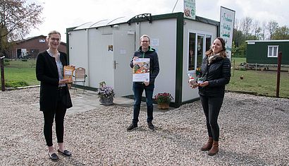 Drei Personen stehen im Freien vor einem Container.