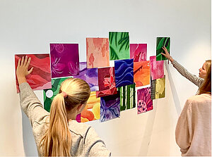 Zwei Schülerinnen hängen ihre selbstgestalteten Bilder an die Wand. 