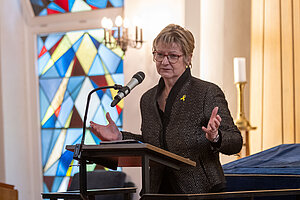 Staatsministerin a.D. Sylvia Löhrmann steht am Rednerpult in der Synagoge in Münster und gestikuliert während ihres Vortrags. 