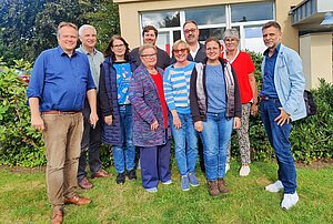 Zehn Frauen und Männer stehen auf einer Rasenfläche vor einem Gebäude. Zehn Frauen und Männer stehen auf einer Rasenfläche vor einem Gebäude.