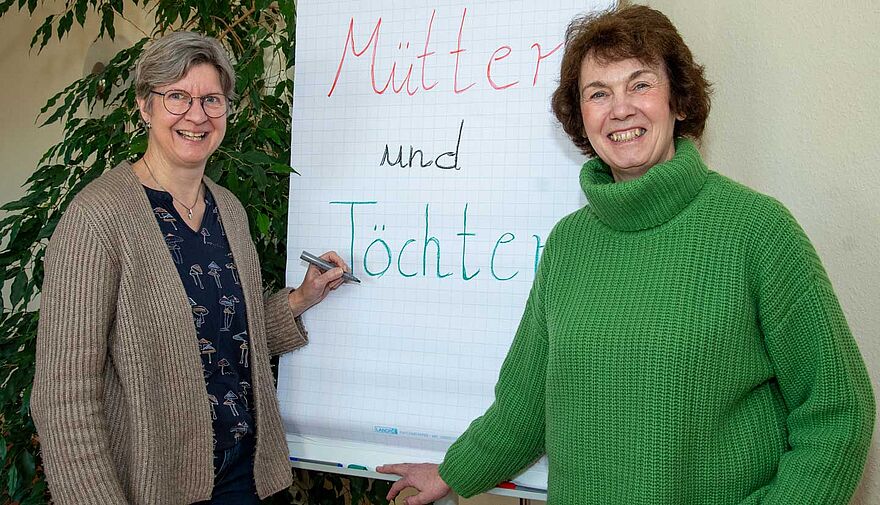 Zwei Frauen stehen vor einem Flipchart mit der Aufschrift "Mütter und Töchter".