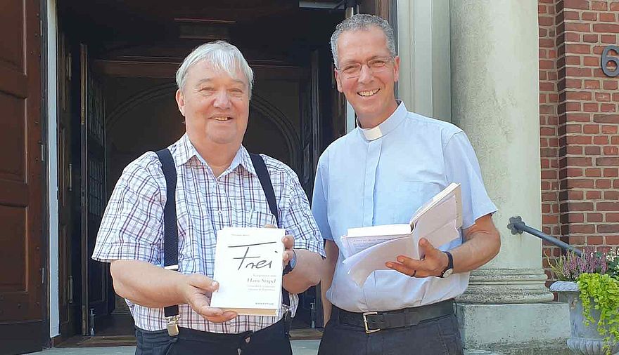 Zwei Männer, die jeweils ein Buch in der Hand halten, stehen vor einem offenen Tor.