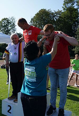 Drei Sportlern auf dem Siegerpodest werden ihre Medaillen überreicht. Drei Sportlern auf dem Siegerpodest werden ihre Medaillen überreicht.