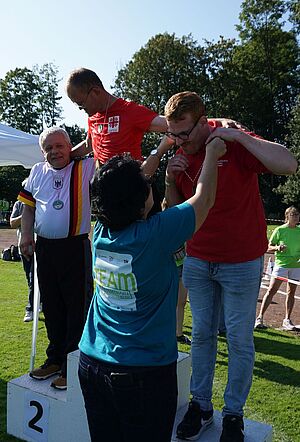 Drei Sportlern auf dem Siegerpodest werden ihre Medaillen überreicht.