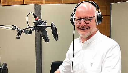 Pfarrer Dr. Jochen reidegeld in einem Tonstudio vor einem Mikrofon. Er trägt einen Kopfhörer. 