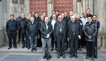 Eine große Gruppe Priester, darunter vorne Kardinal Omella und Bischof Genn, steht vor dem Portal des St.-Viktor-Doms in Xanten.