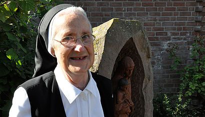 Schwester Rita steht im Garten des St.-Josef-Hauses, im Hintergrund ist eine Marienstatue 