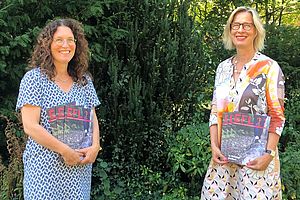 Andrea Beer und Andrea Stachon-Groth stehen in einem Garten und halten mehrere Exemplare des Jahresberichtes in den Händen. 