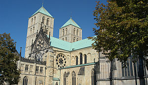 Blick vom Domplatz auf das Paradiesportal des St. Paulus-Doms MÜnster. Auf dem Domplatz stehen grün-belaubte Bäume.