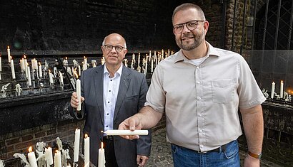 Zwei Männer stehen an einem Kerzenständer und entzünden jeweils eine Kerze.